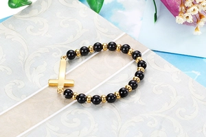 Détail d'un bracelet de perles noires brillantes avec un pendentif croix dorée