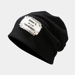 Close-up of black knitted slouchy beanie with vintage raw-edge patch and printed text