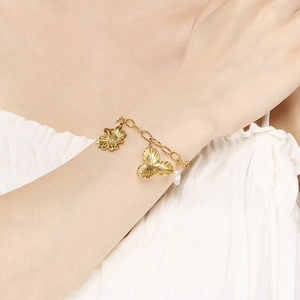 Detail of a gold floral charm bracelet with a daisy, leaf pendant, and small white pearl