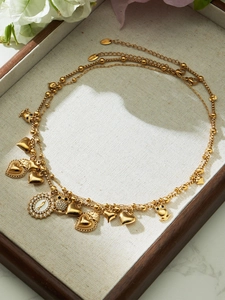 Detail of layered gold stainless steel necklace with owl and icon pendants on tray