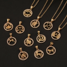 Close-up of gold zodiac necklaces with sparkling pavé crystals on a black background