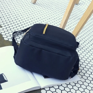 Minimalist black mini backpack with gold zippers shown on a stylish white honeycomb floor