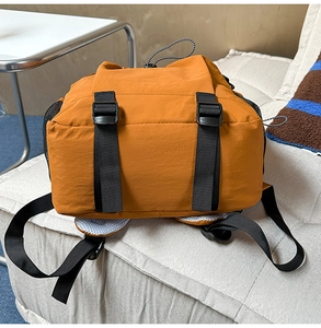 Detailaufnahme des orangebraunen Nylon-Rucksacks mit schwarzen Gurten auf dem Sofa