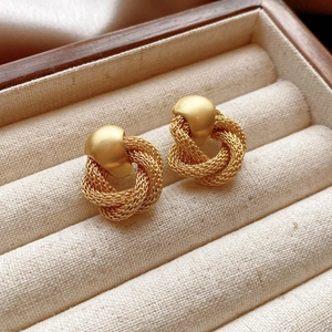 Macro shot of gold woven twist hoop earrings with matte stud in a wooden jewelry box