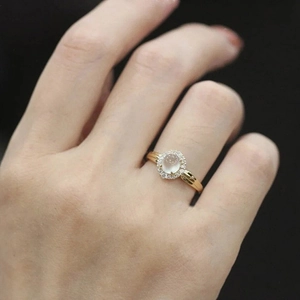 Detailed view of a gold moonstone ring with a diamond halo on a finger