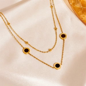Detail of gold double-layer necklace with black Roman numeral pendant on beige silk