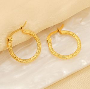 Close-up of gold plated spiral hoop earrings with elegant twisted texture on marble