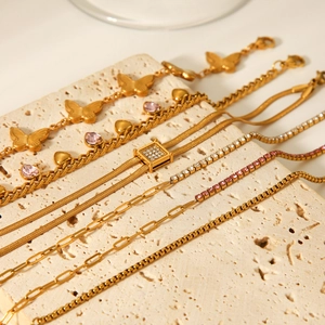 Detailed display of gold butterfly and heart charm bracelets on beige travertine stone