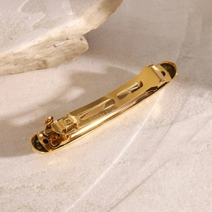 Close-up of golden metallic spring hair clip with Clip France engraving on stone background
