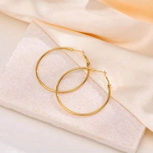 Detailed view of polished gold stainless steel hoop earrings on elegant silk background