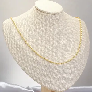 Polished gold wave chain necklace displayed on a jewelry stand with satin fabric