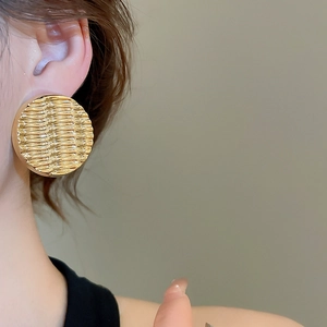 Detailed view of large gold circular stud earrings with unique 3D water ripple texture
