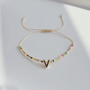 Detail eines böhmischen Perlenarmbands mit goldenem V-Anhänger auf minimalistischem Hintergrund