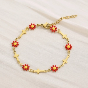Detail of gold chain bracelet with red daisy and cross charms on beige fabric