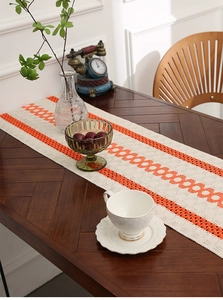 Detail of two-tone woven table runner in cream and orange on a wooden dining table
