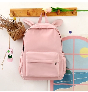 Detailed close-up of pink school backpack with bunny ears hanging on a wooden wall hook