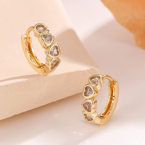 Close-up of gold heart hoop earrings with sparkling zircon stones on a beige pedestal