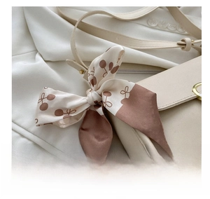 Close-up of a printed silk scarf tied as a bow on a beige leather handbag strap