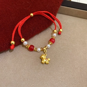Dettaglio del bracciale intrecciato rosso con ciondolo a cavallo dorato e perle