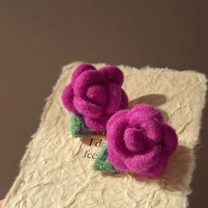 Detailed close-up of handmade magenta felt flower earrings with green leaves