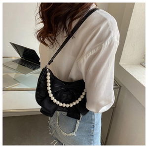 Detail of black bow shoulder bag with white pearl strap shown on model in modern setting