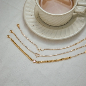 Detailed view of three gold zirconia bracelets with heart and heartbeat charms on white fabric