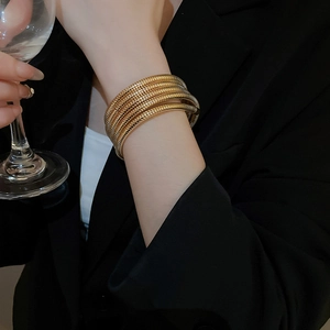 Detailed view of multilayer spiral gold bangle worn with formal attire and glassware