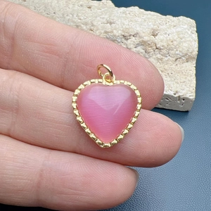 Golden heart pendant featuring a pink cat eye stone and textured edges held in hand