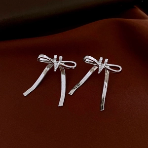 Detailed view of silver bow earrings with zircon stones and long hanging snake chain tassels