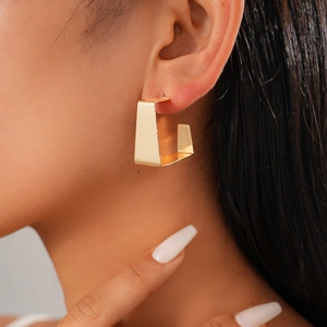 Detail of a minimalist gold geometric earring showing a polished rectangular metal finish