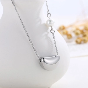 Détail d'un collier argenté avec pendentif cœur et perle sur un vase blanc