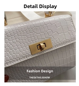 Close-up of white crocodile embossed texture and golden rectangular twist lock on handbag