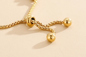 Macro shot of gold box chain jewelry featuring adjustable sliding bead and ball charms