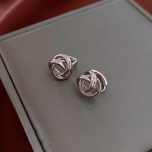 Close-up of silver knotted stud earrings on grey velvet display with red silk accents