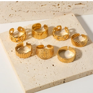 Set of 7 gold stainless steel rings with various textures on a beige stone surface