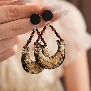 Close-up of vintage resin crescent earring with gold foil details and beaded chain