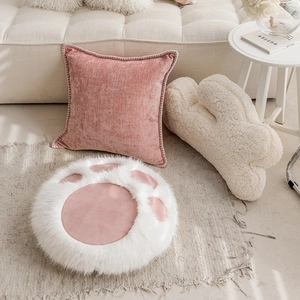 Pink velvet square cushion and white plush cat paw seat pad on a cozy modern sofa