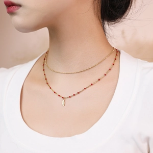 Detail view of double-layer gold feather pendant necklace with elegant red beads on neck