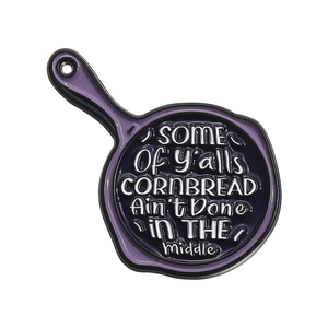 Skillet enamel pin with purple rim featuring humoristic cornbread quote on a white background