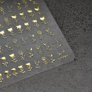 Detail-Makroaufnahme von 3D-Goldpräge-Nagelstickern mit Rosenmotiven auf dunklem Stein