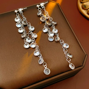 Detailed view of silver tassel earrings with round cubic zirconia on brown leather case