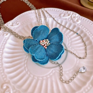Gros plan du collier fleur en denim bleu avec chaîne argentée et pendentif zircon