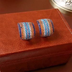Dettaglio macro di orecchini a lobo curvi con zirconi arcobaleno su astuccio in pelle