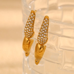 Close-up of gold U-shaped earrings with micro-pave crystals on transparent glass