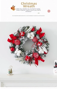 Christmas wreath with red baubles, bow and faux snow hanging on a white wall