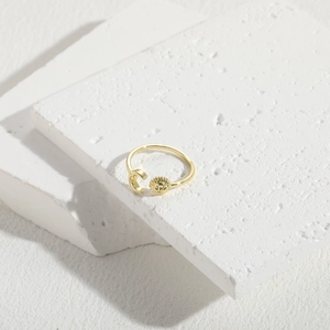 Detail of gold open ring featuring sun and moon charms on white natural stone