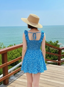 Detail of blue floral sundress with ruffle straps and tie back against a seaside background