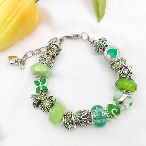 Silver bracelet with green rhinestone, glass, and clover beads on white fabric