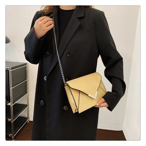Detail of pale yellow envelope crossbody bag with metal chain strap on black coat