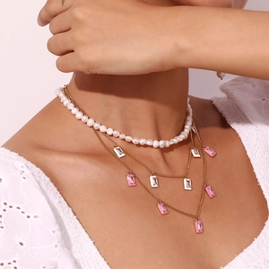 Detail of layered gold necklace with white pearls and pink rectangular enamel pendant